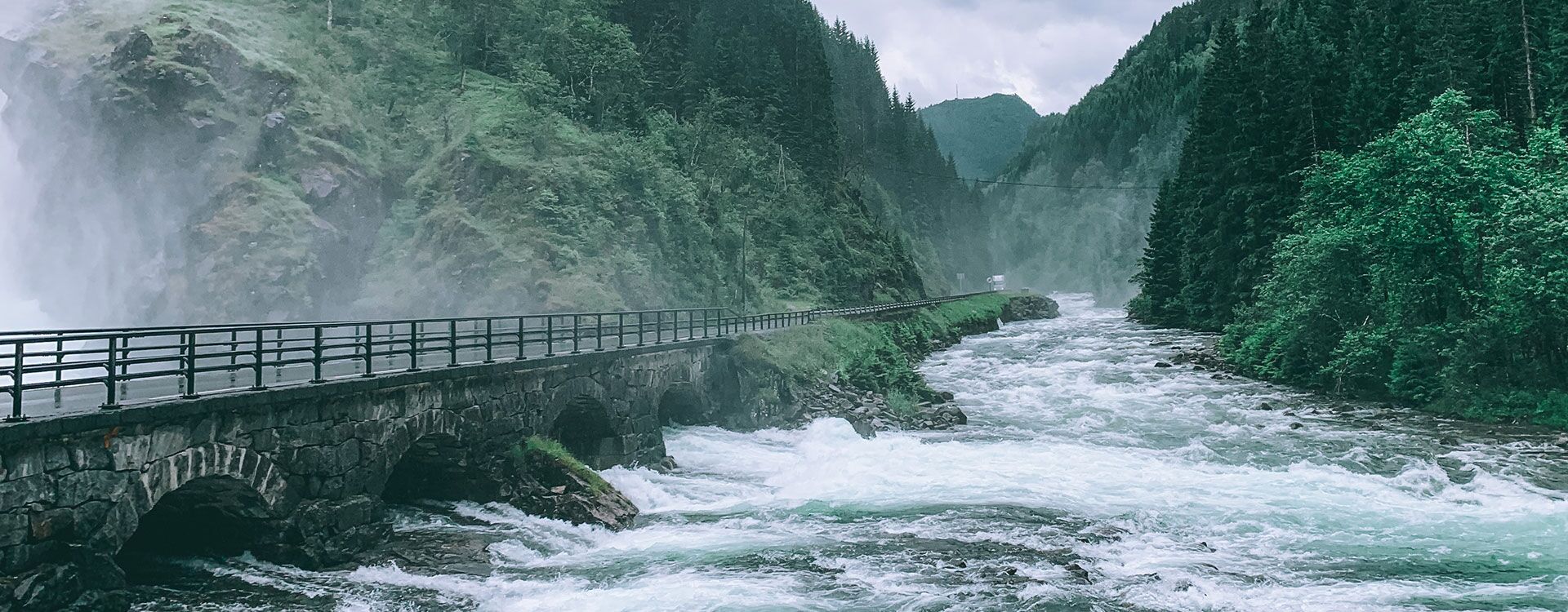 Steinbrücke, die über einen sprudelnden Fluss führt, umgeben von Wald