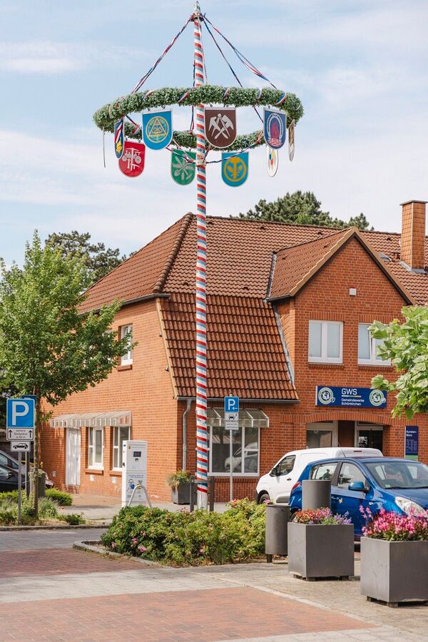 aufgestellter Maibaum, im Hintergrund das Gebäude der Gemeindewerke Schönkirchen