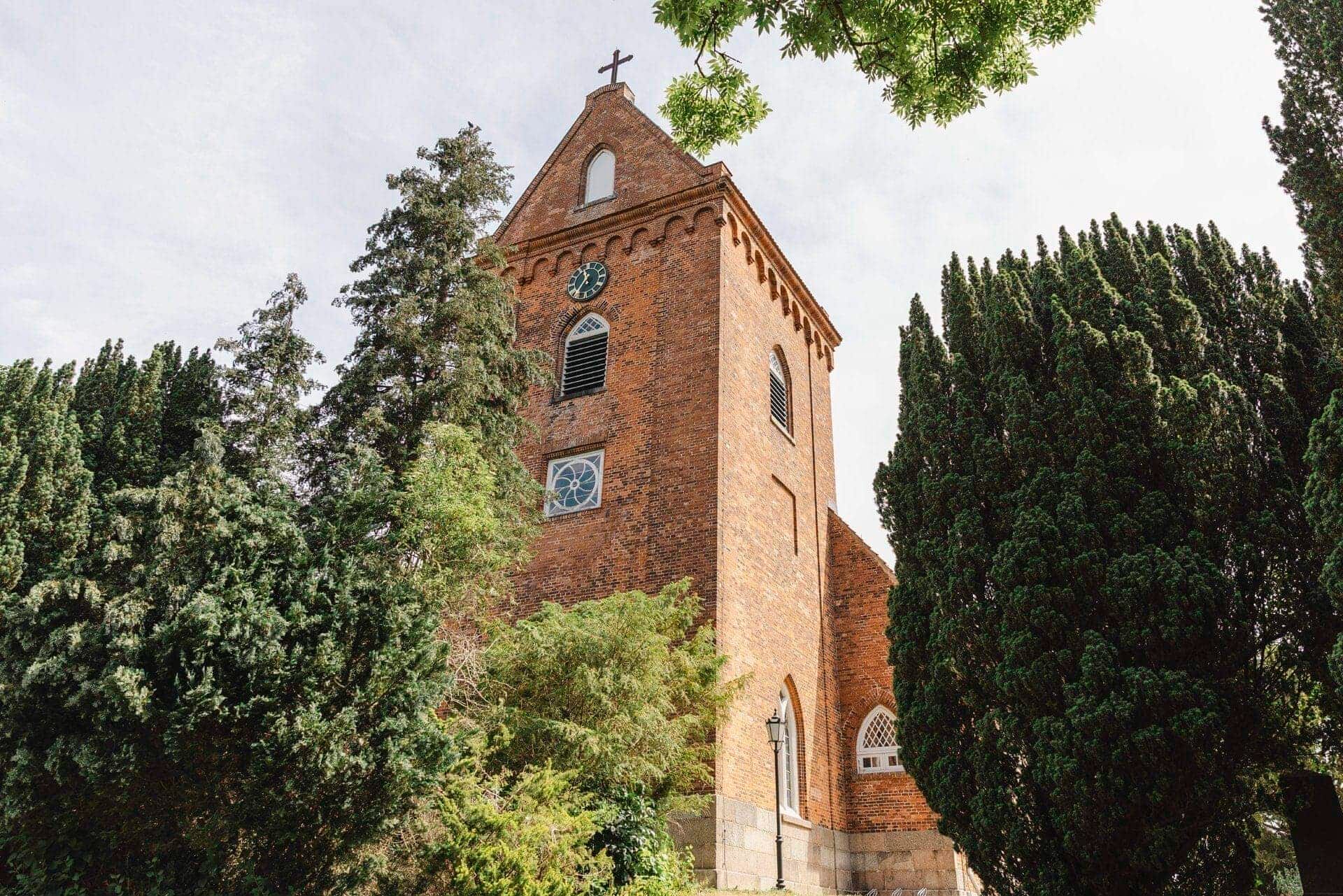 Kirchturm mit davorstehenden großen Bäumen in Schönkirchen