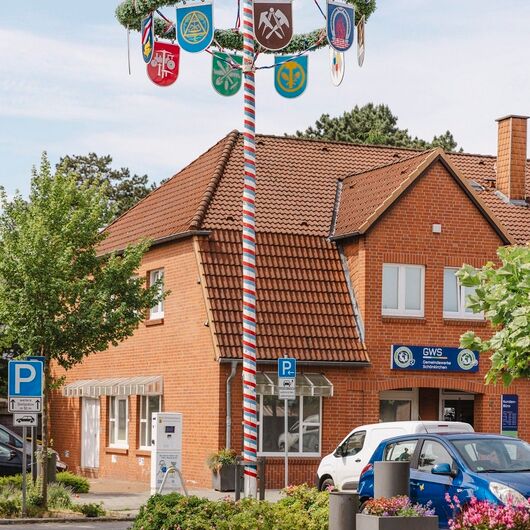 aufgestellter Maibaum, im Hintergrund das Gebäude der Gemeindewerke Schönkirchen