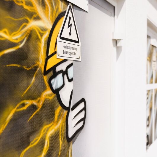 Graffiti eines Bauarbeiters mit Helm, um den elektrische Blitze schweben und der um die Ecke einer Tür schaut