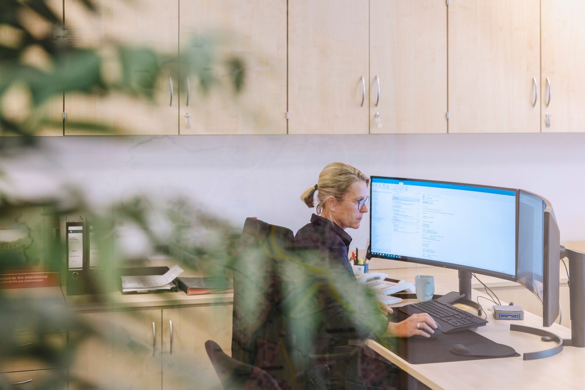 Büro-Mitarbeiterin, die am Rechner mit zwei großen Monitoren sitzt und Daten bearbeitet