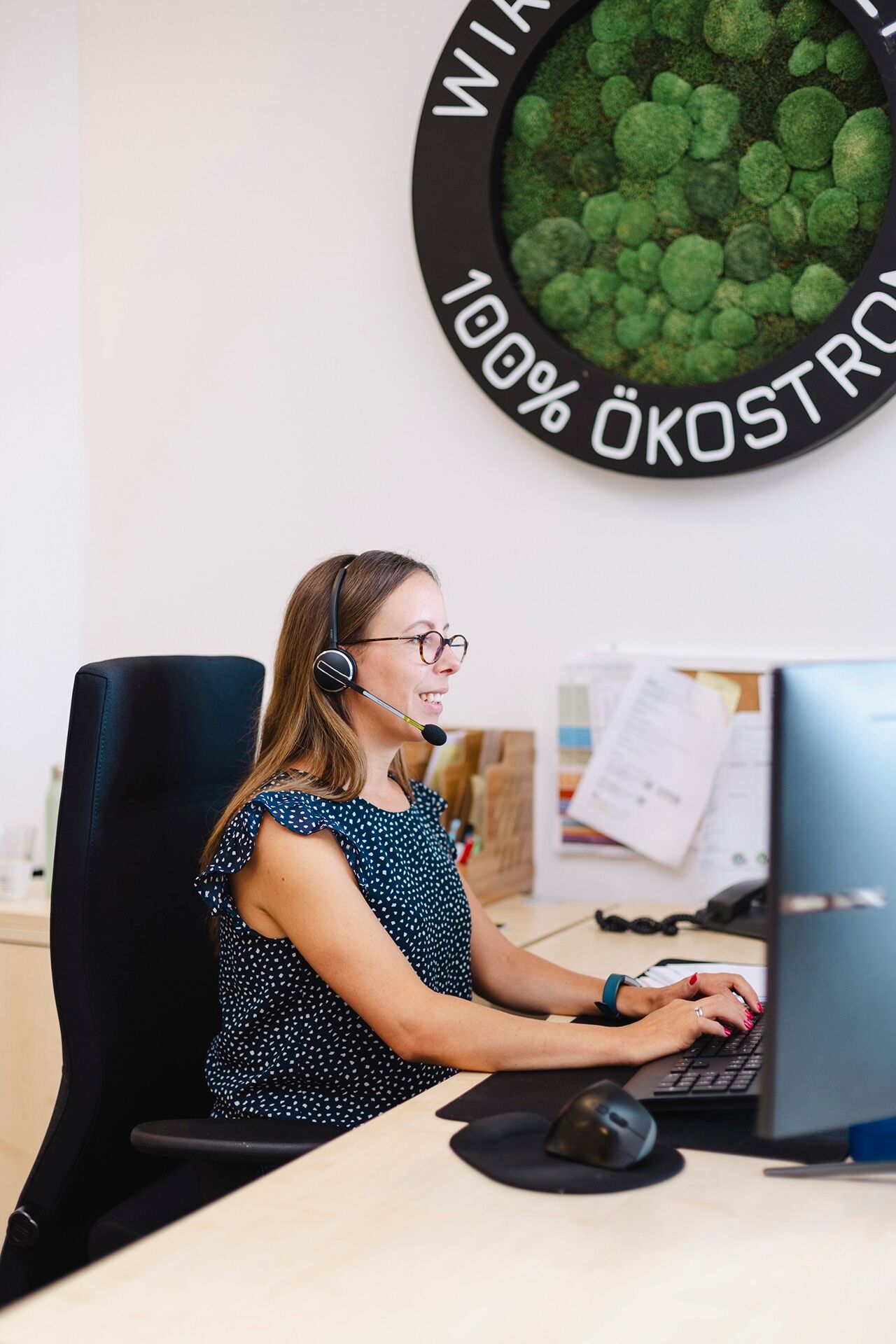 Mitarbeiterin mit Headset, die am Rechner sitzt und freundlich lächelt