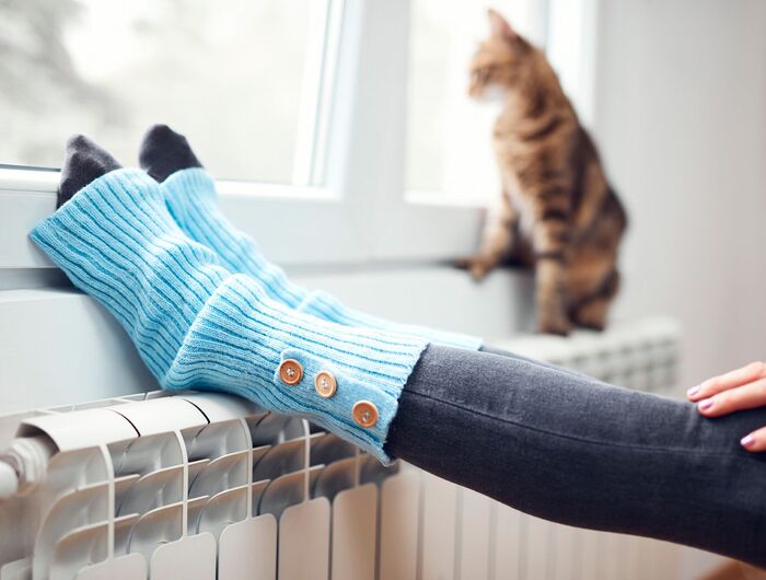 Füße in Stulpen, die auf einer Heizung liegen, im Hintergrund eine Katze
