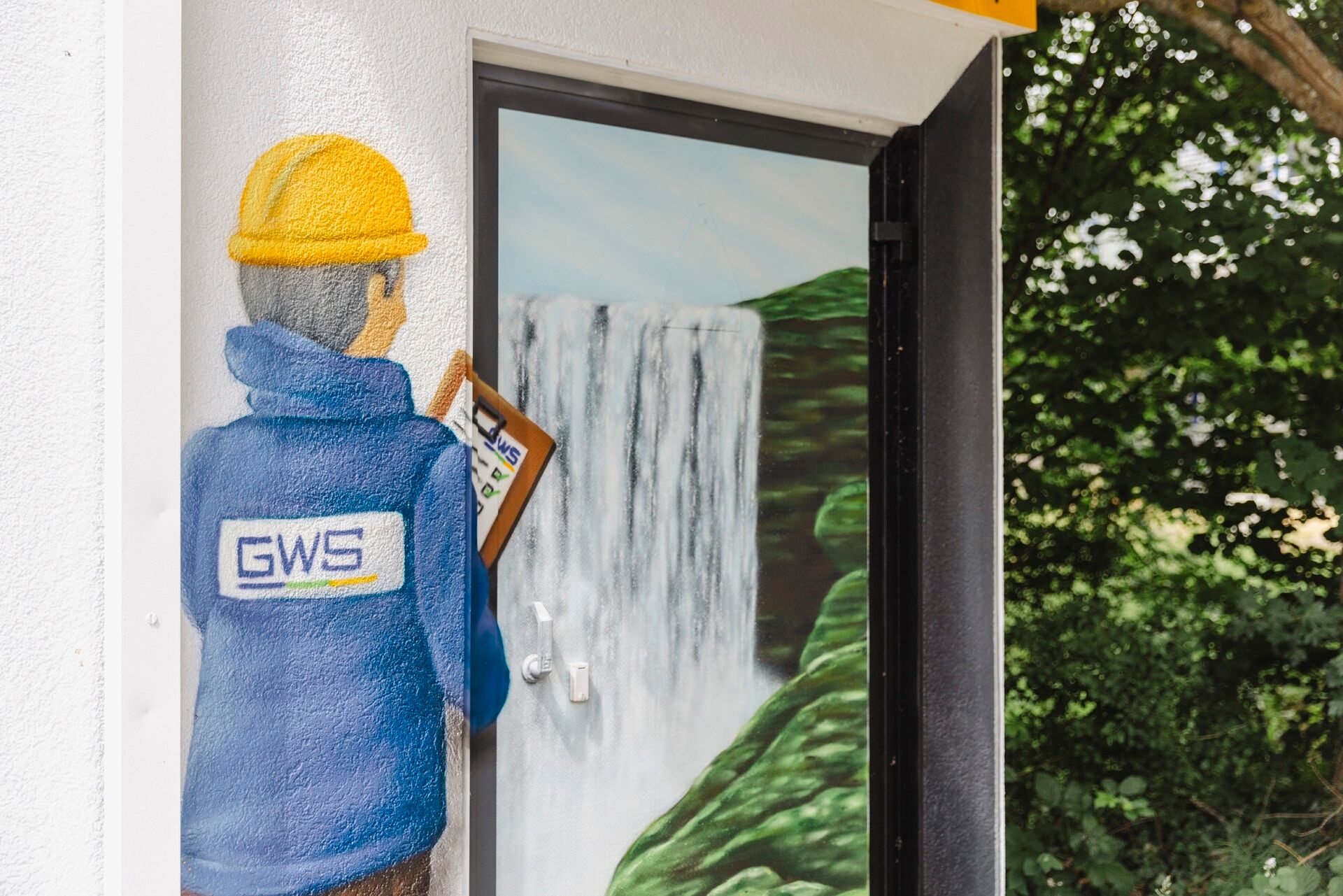Teil-Aufnahme eines Graffitis, das einen Mitarbeiter mit GWS-Jacke, Helm und Klemmbrett zeigt, der auf einen Wasserfall schaut