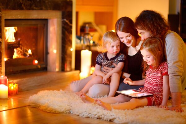 Familie mit zwei Kindern sitzen auf einem Fell umgeben von Kerzen und schauen gemeinsam auf ein Tablet
