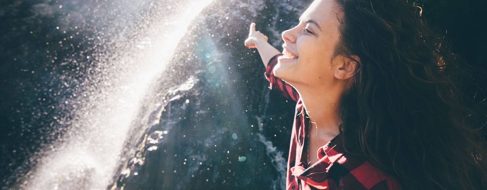 Lachende, junge Frau, die unter den Wassertropfen eines Wasserfalls steht